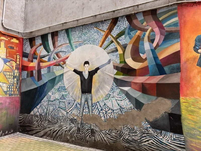Zdjęcie przedstawia kolorowe podwórka i mural z chłopcem, który ma otwarte ramiona i jest otoczony przez abstrakcyjne figury i linie.