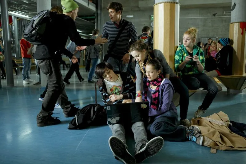 Kadr z filmu przedstawiający młodzież szkolną podczas przerwy spoglądającą na ekran laptopa