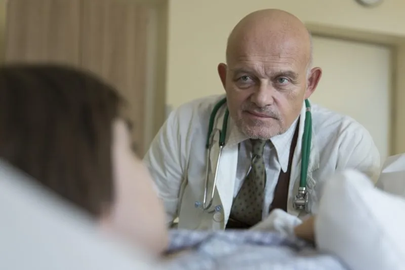 Doktor obserwujący chłopca leżącego na łóżku szpitalnym.