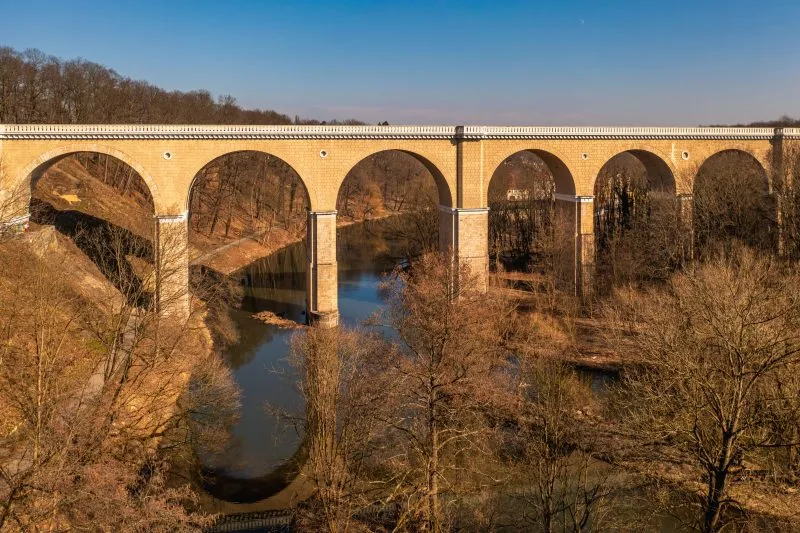 Zdjęcie przedstawia monumentalny, kamienny most kolejowy w Zgorzelcu o łukowej konstrukcji, który wznosi się nad Nysą Łużycką