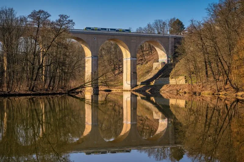 Zdjęcie przedstawia monumentalny, kamienny most kolejowy w Zgorzelcu o łukowej konstrukcji, który wznosi się nad Nysą Łużycką
