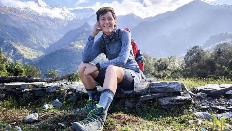 Anna Możdżonek sedí na kamenné zídce v turistickém oblečení, s batohem a holí v ruce, a za ní se rozprostírá vysoký horský masiv.