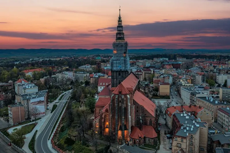 Imponująca budowla z wysokimi, strzelistymi wieżami, których szczyty sięgają nieba, a na tle nieba wyróżnia się gotycka fasada, ozdobiona bogatymi detalami i witrażami, z majestatycznymi przyporami podpierającymi mur.