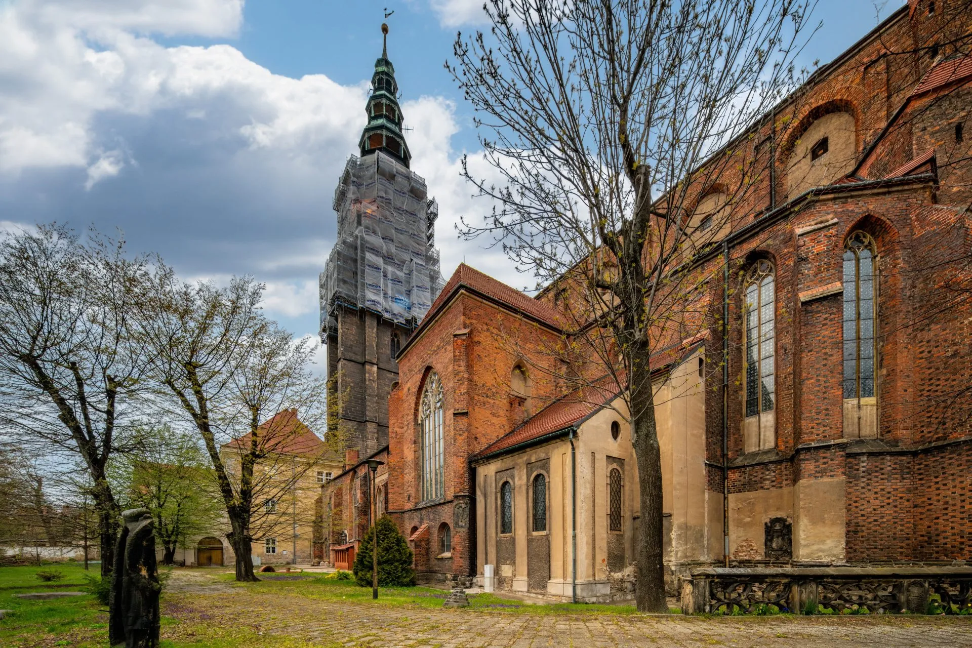 Imponująca budowla z wysokimi, strzelistymi wieżami, których szczyty sięgają nieba, a na tle nieba wyróżnia się gotycka fasada, ozdobiona bogatymi detalami i witrażami, z majestatycznymi przyporami podpierającymi mur.