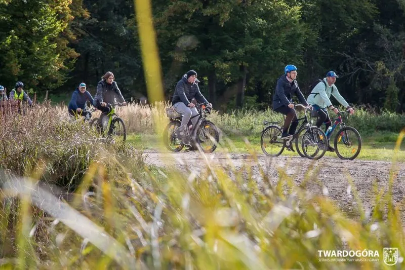 Skupina cyklistů jede po nové stezce pro pěší a cyklisty z Goszcze do Domasławic a přejíždí slunnou mýtinu na okraji lesa.