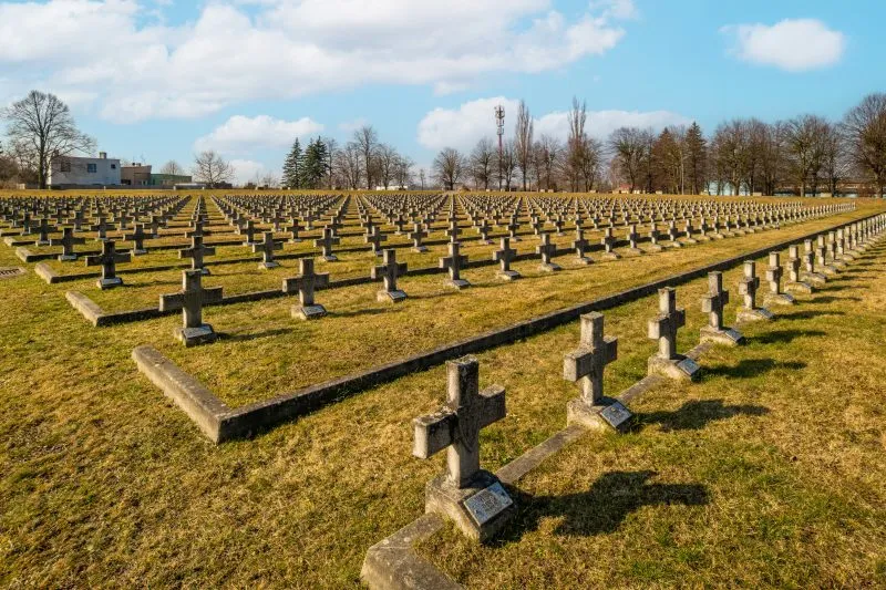 Na zdjęciu widać uporządkowany cmentarz z kamiennymi nagrobkami, otoczony zielenią, z zadbaną przestrzenią upamiętniającą żołnierzy II Armii Wojska Polskiego.
