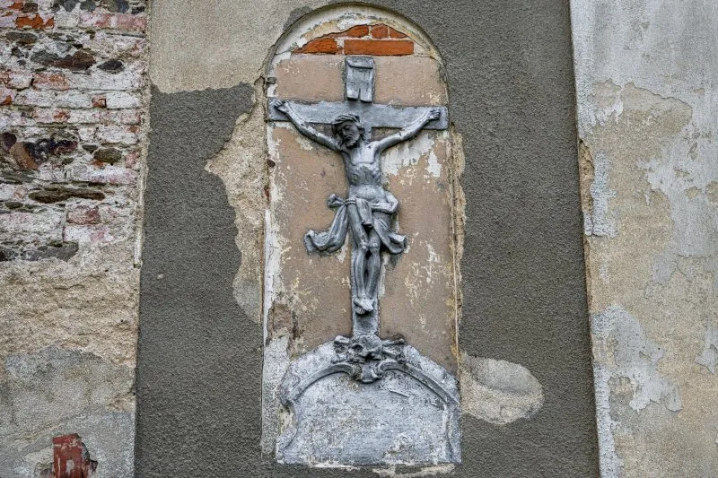 Na zdjęciu widać krzyż z figurą Jezusa umieszczony na ścianie kościoła św. Mikołaja, wyróżniający się na tle ceglanej elewacji świątyni.