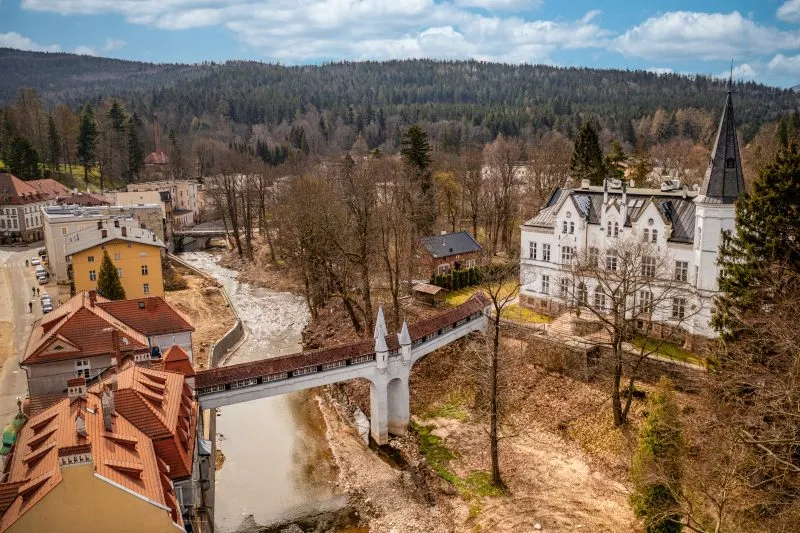 Kryty Most w Lądku-Zdroju to zabytkowa kamienna konstrukcja z łukowym przejściem, przykryta drewnianym dachem, otoczona bujną roślinnością i malowniczym krajobrazem.
