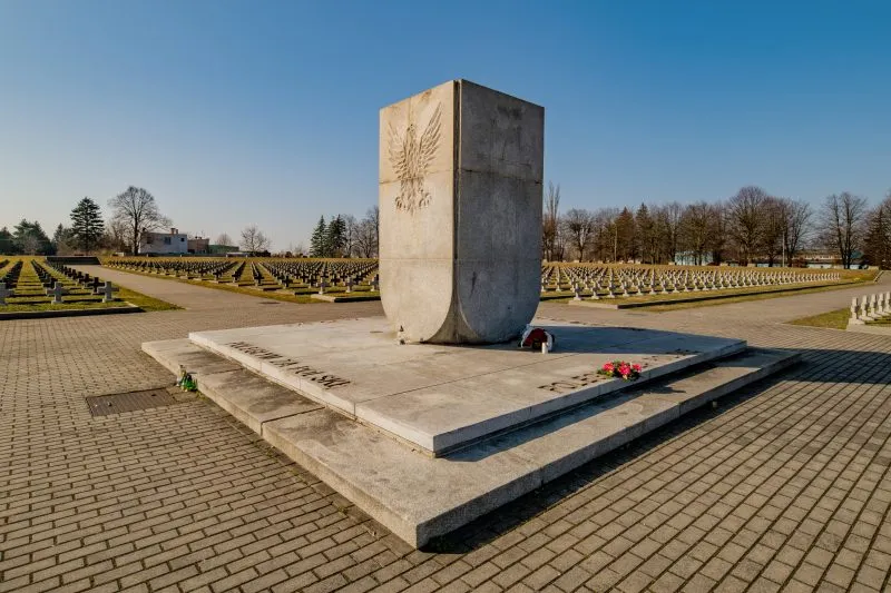 Na zdjęciu widać uporządkowany cmentarz z kamiennymi nagrobkami, otoczony zielenią, z zadbaną przestrzenią upamiętniającą żołnierzy II Armii Wojska Polskiego.
