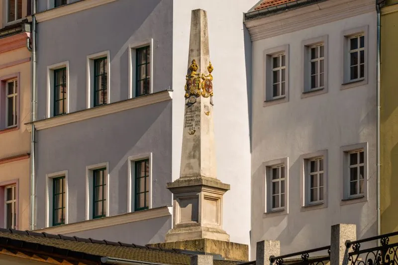 Kamienny, barokowy słup z herbami i inskrypcjami wskazującymi odległości do miast.