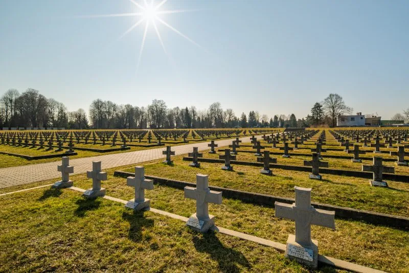 Na zdjęciu widać uporządkowany cmentarz z kamiennymi nagrobkami, otoczony zielenią, z zadbaną przestrzenią upamiętniającą żołnierzy II Armii Wojska Polskiego.
