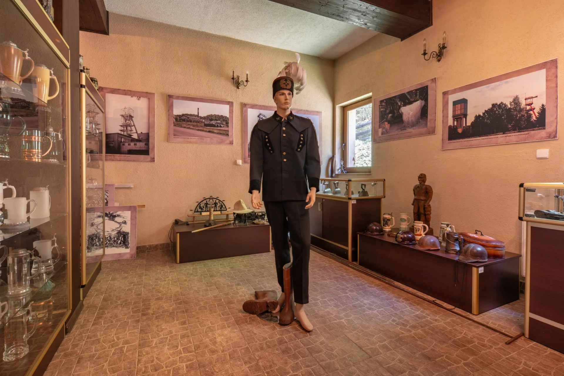 Wnętrze muzeum z manekinem ubranym w tradycyjny strój górniczy i eksponatami dotyczącymi historii górnictwa na ścianach i w gablotach.