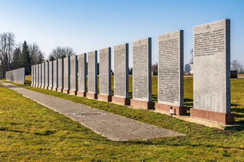 Na zdjęciu widać uporządkowany cmentarz z kamiennymi nagrobkami, otoczony zielenią, z zadbaną przestrzenią upamiętniającą żołnierzy II Armii Wojska Polskiego.
