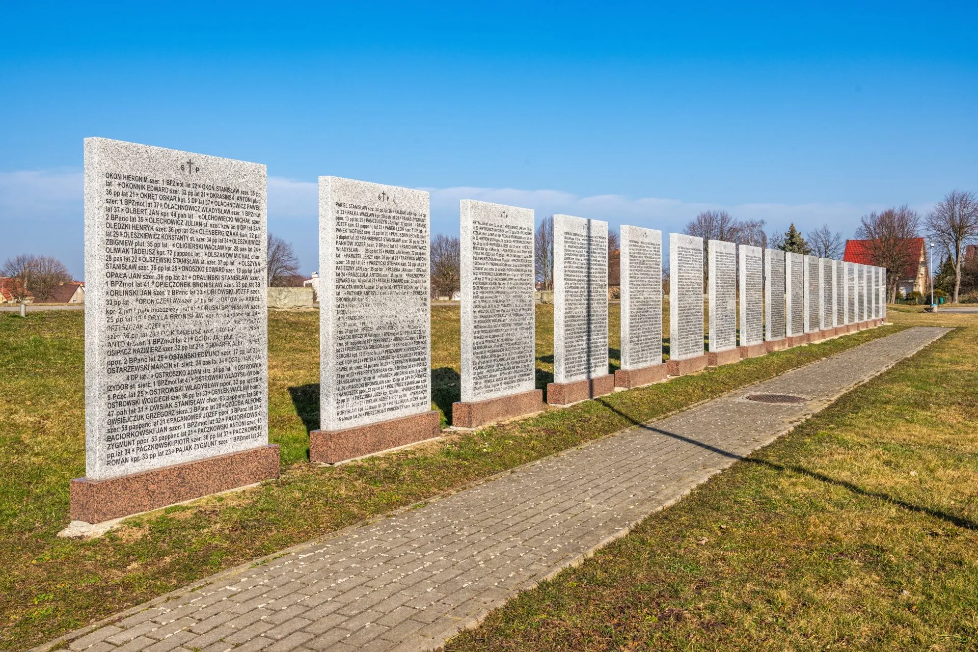 Na zdjęciu widać uporządkowany cmentarz z kamiennymi nagrobkami, otoczony zielenią, z zadbaną przestrzenią upamiętniającą żołnierzy II Armii Wojska Polskiego.

