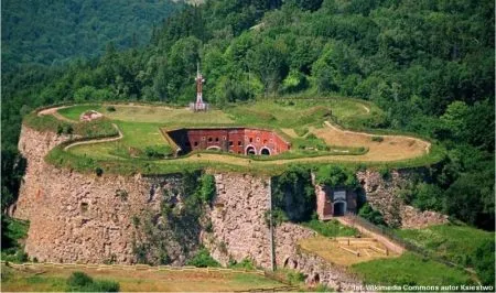 Twierdza Srebrna Góra widziana z lotu ptaka ukazuje kamienne bastiony, ceglane koszary i ziemne fortyfikacje otoczone gęstymi lasami Gór Sowich.