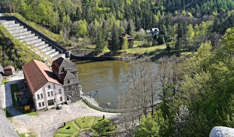 Elektrownia wodna i zapora w Pilchowicach widziane z góry, nad zielonkawą taflą Bobru, pośród stromych zboczy porośniętych gęstym lasem.