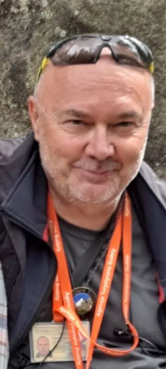 Jarosław Czerkawski se usmívá na portrétní fotografii v exteriéru, má brýle na hlavě, tmavou bundu a oranžovou šňůrku na krk s identifikační kartou.
