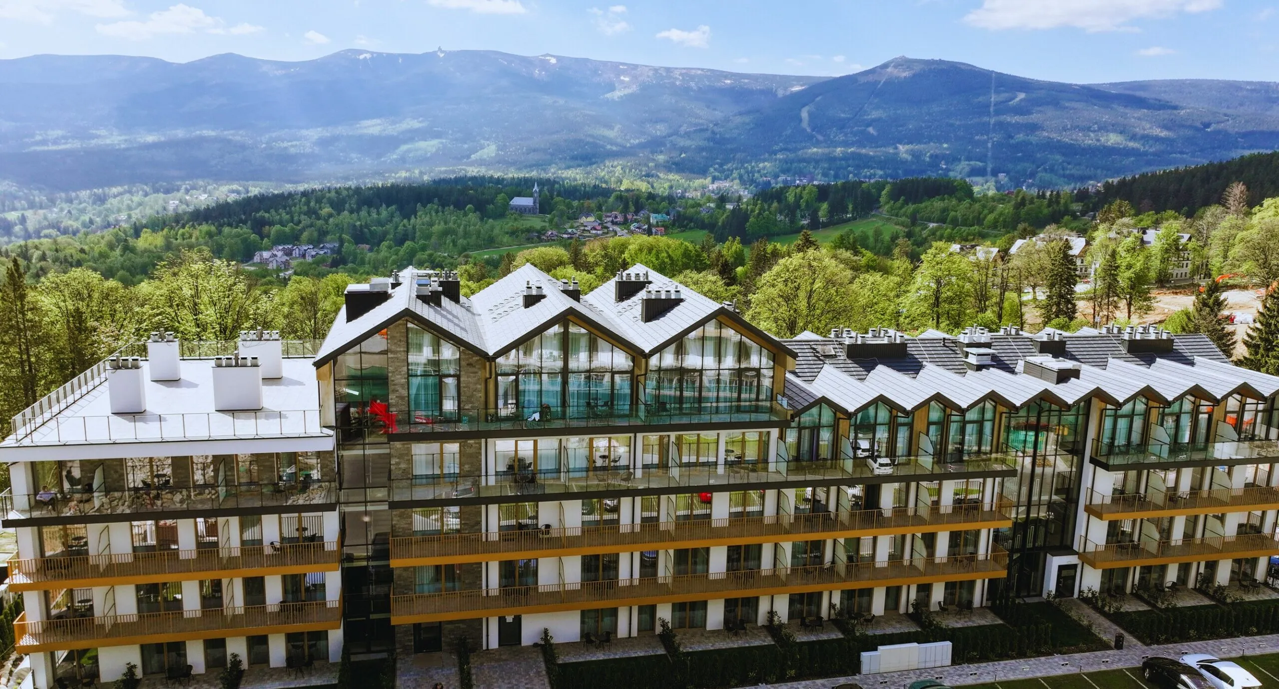 Widok z lotu ptaka na resort - elegancki budynek o przytulnym górskim charakterze, z dużymi oknami i balkonami, w tle góry.