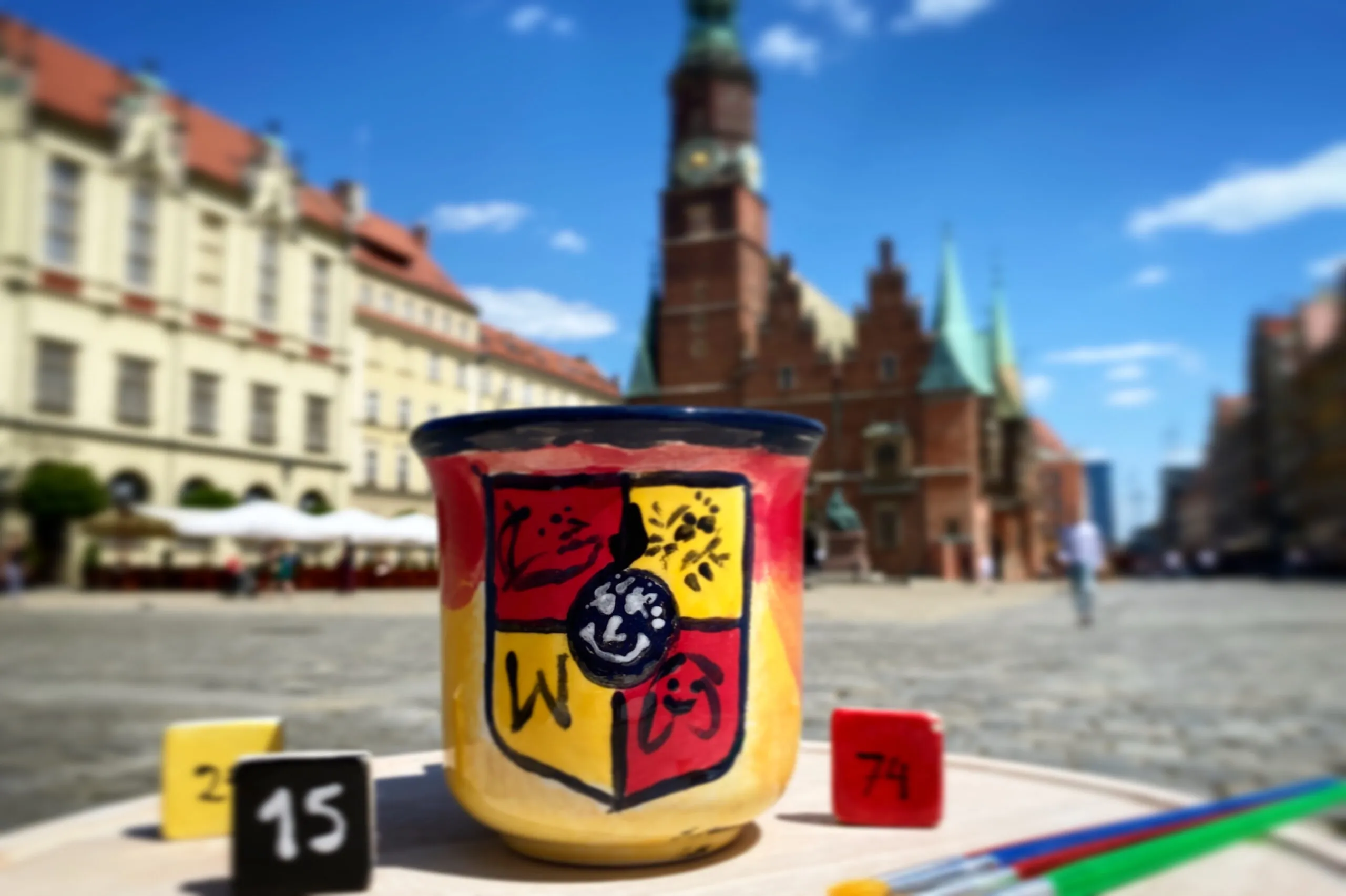 Pomalowany kubek w herb Wrocławia- żółto-czerwony na tle wrocławskiego ratusza