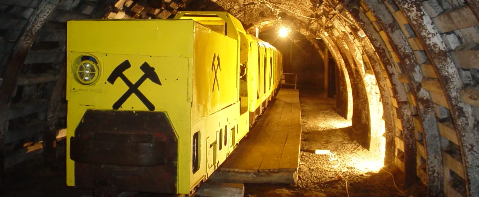 Żółte wagoniki kolei w oświetlonym tunelu kopalni.