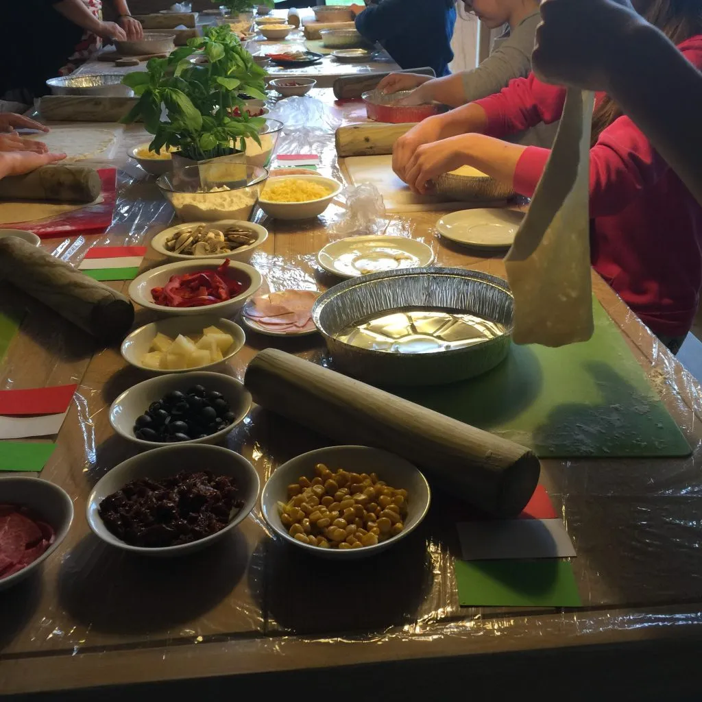 Przygotowanie pizzy na style- leżące ciasto oraz składniki, obok leżą miniatury włoskiej flagi