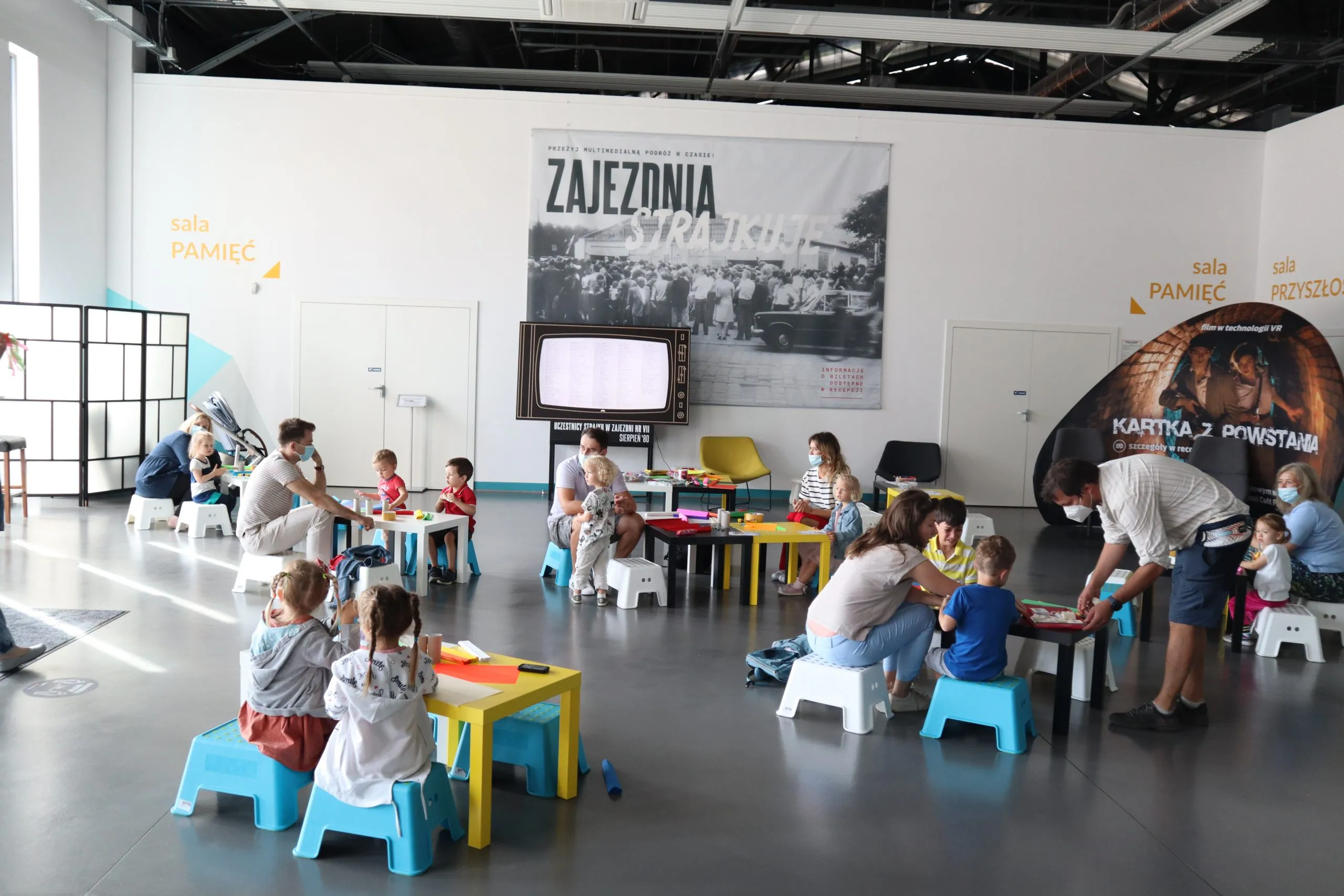 Grupa dzieci siedzi w salce przy małych stolikach wycinając rzeźby z papieru