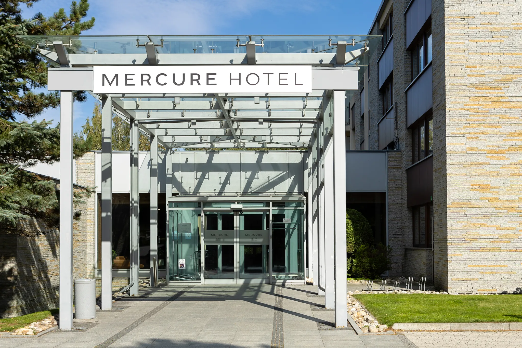 Szklany daszek prowadzi do głównego wejścia hotelu, podkreślając jego nowoczesny i elegancki charakter. Otoczenie budynku jest starannie utrzymane i harmonijnie wpisuje się w górski krajobraz.