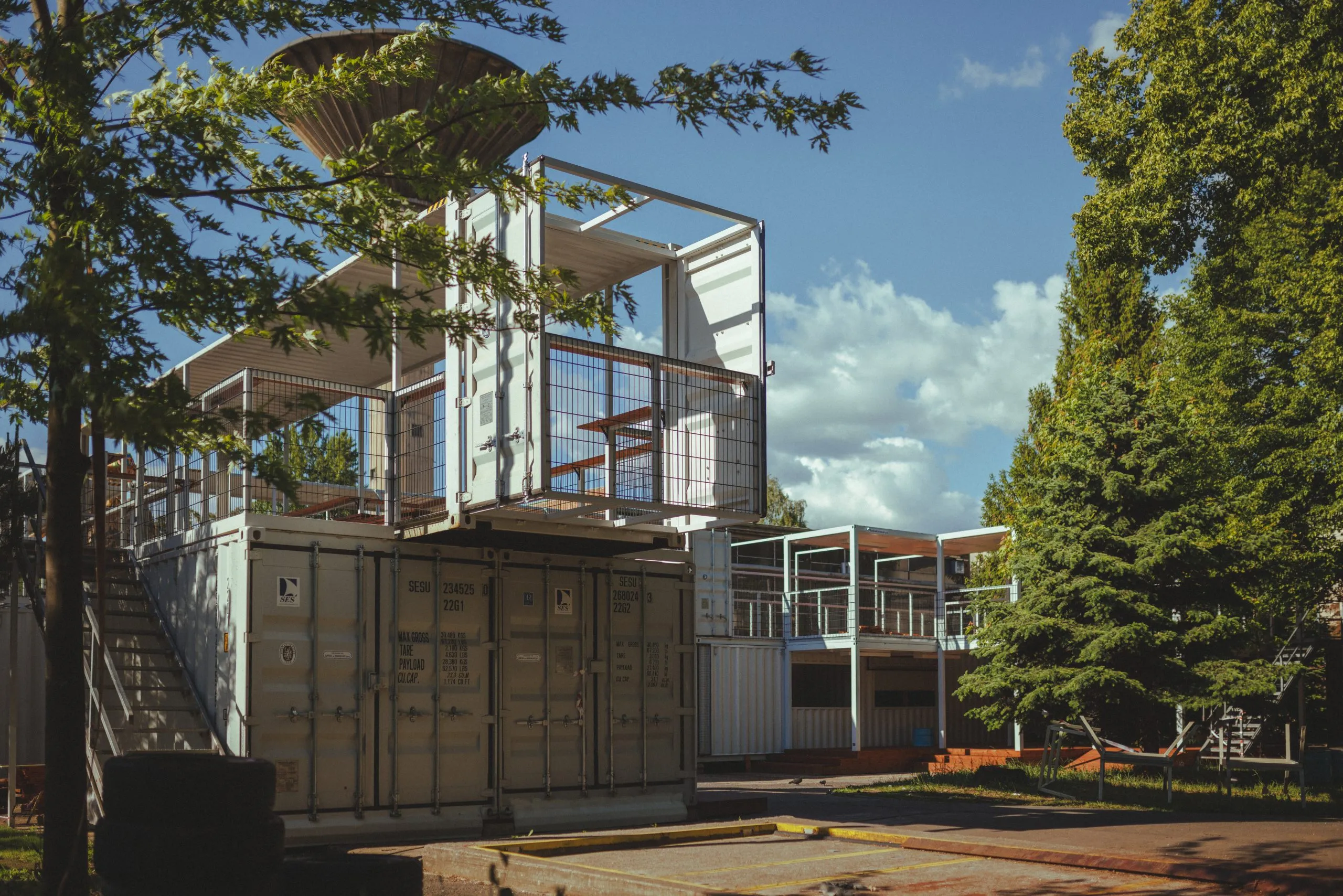 Zdjęcie przedstawia metalową instalację w otoczeniu kontenerów i starej fabryki
