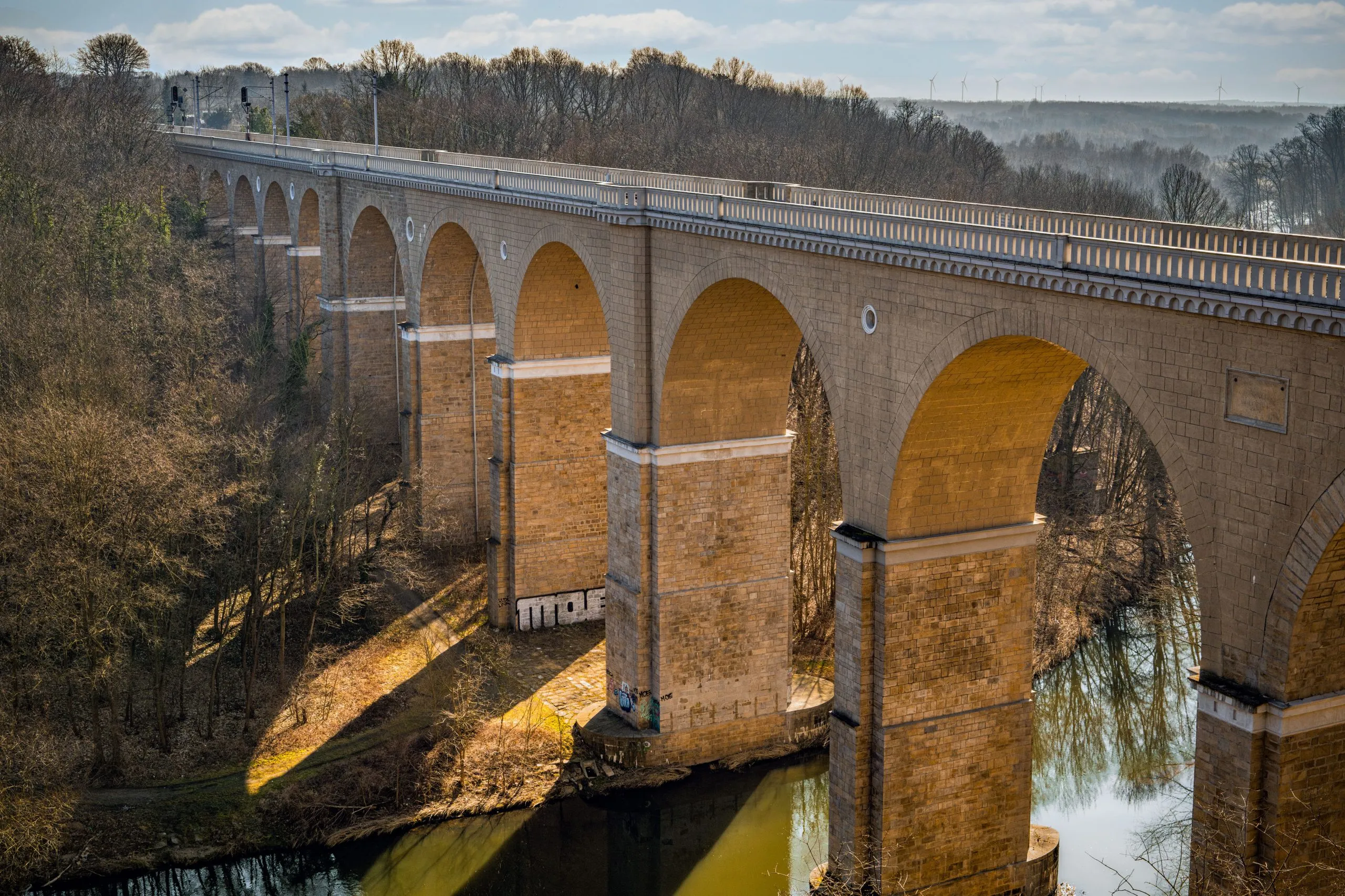 Zdjęcie przedstawia monumentalny, kamienny most kolejowy w Zgorzelcu o łukowej konstrukcji, który wznosi się nad Nysą Łużycką.
