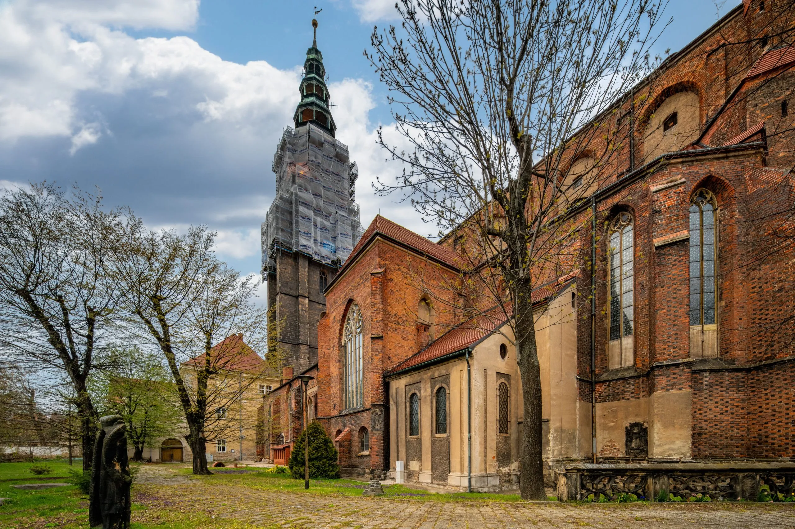 Imponująca budowla z wysokimi, strzelistymi wieżami, których szczyty sięgają nieba, a na tle nieba wyróżnia się gotycka fasada, ozdobiona bogatymi detalami i witrażami, z majestatycznymi przyporami podpierającymi mur.