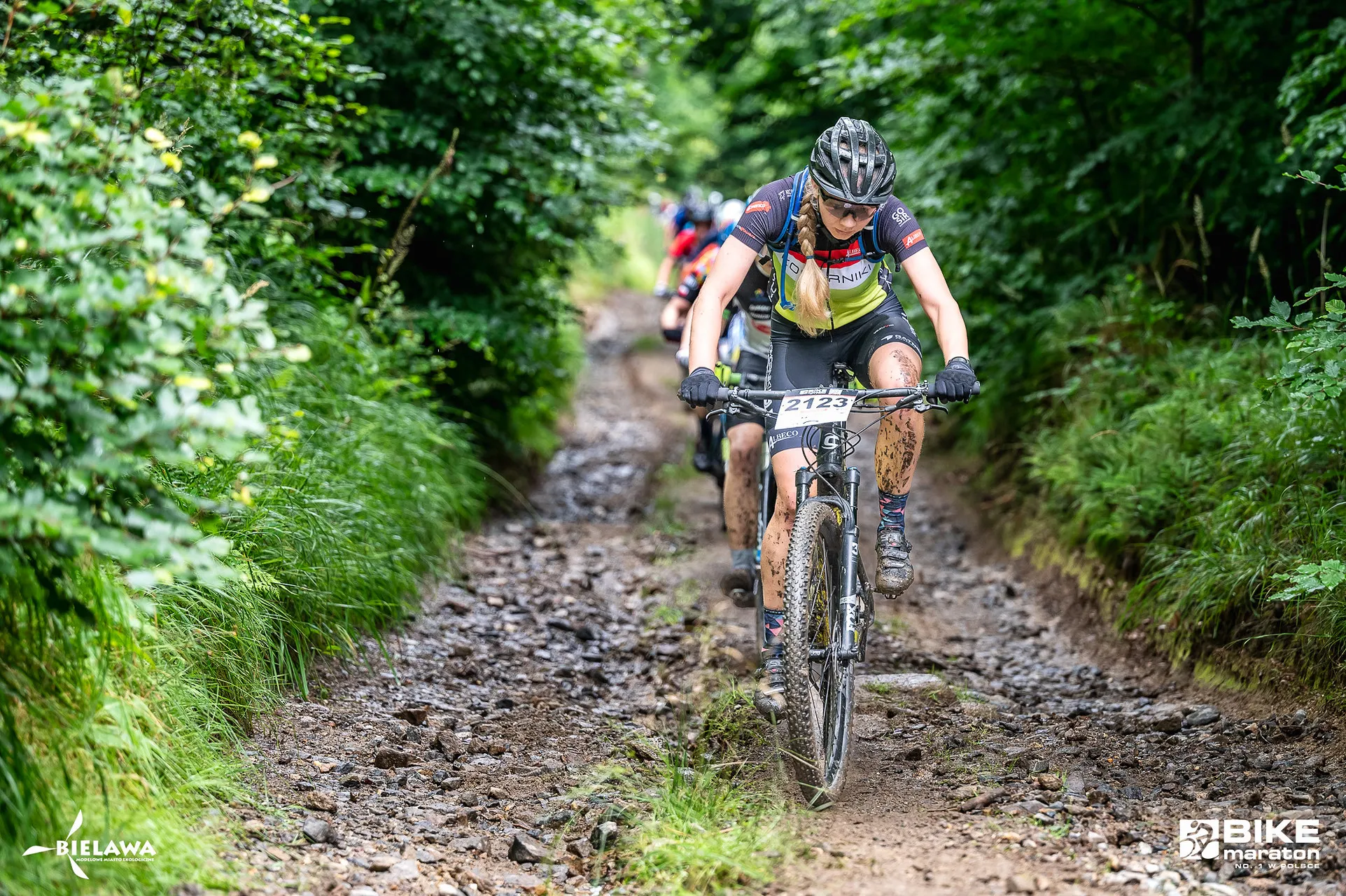 Kolarz górski zjeżdża kamienistą, błotnistą ścieżką między gęstymi krzewami podczas Bike Maratonu w Bielawie w Górach Sowich.
