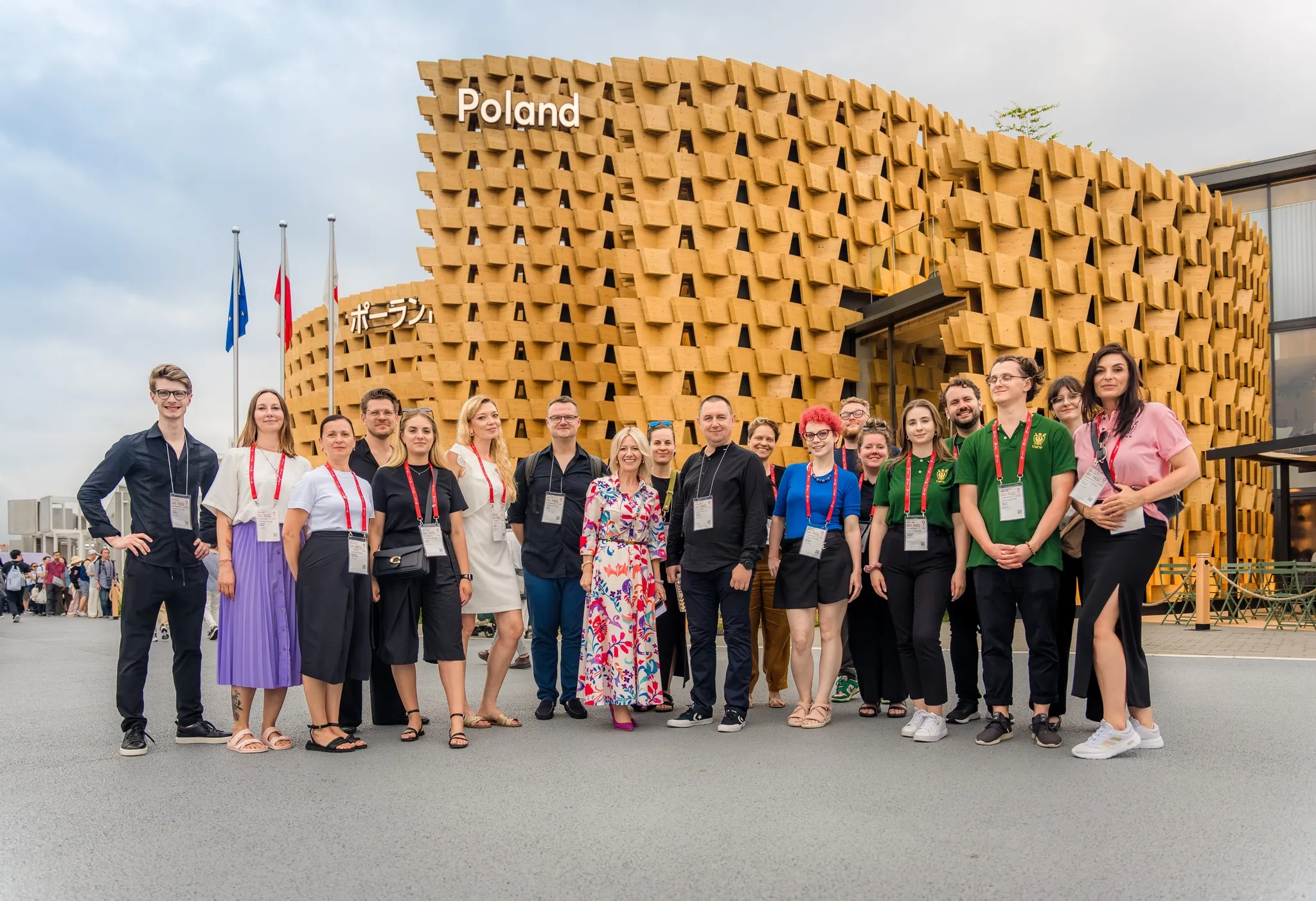 Uczestnicy dolnośląskiej prezentacji na Expo Osaka 2025 pozują przed drewnianą fasadą Pawilonu Polski, trzymając regionalne flagi.