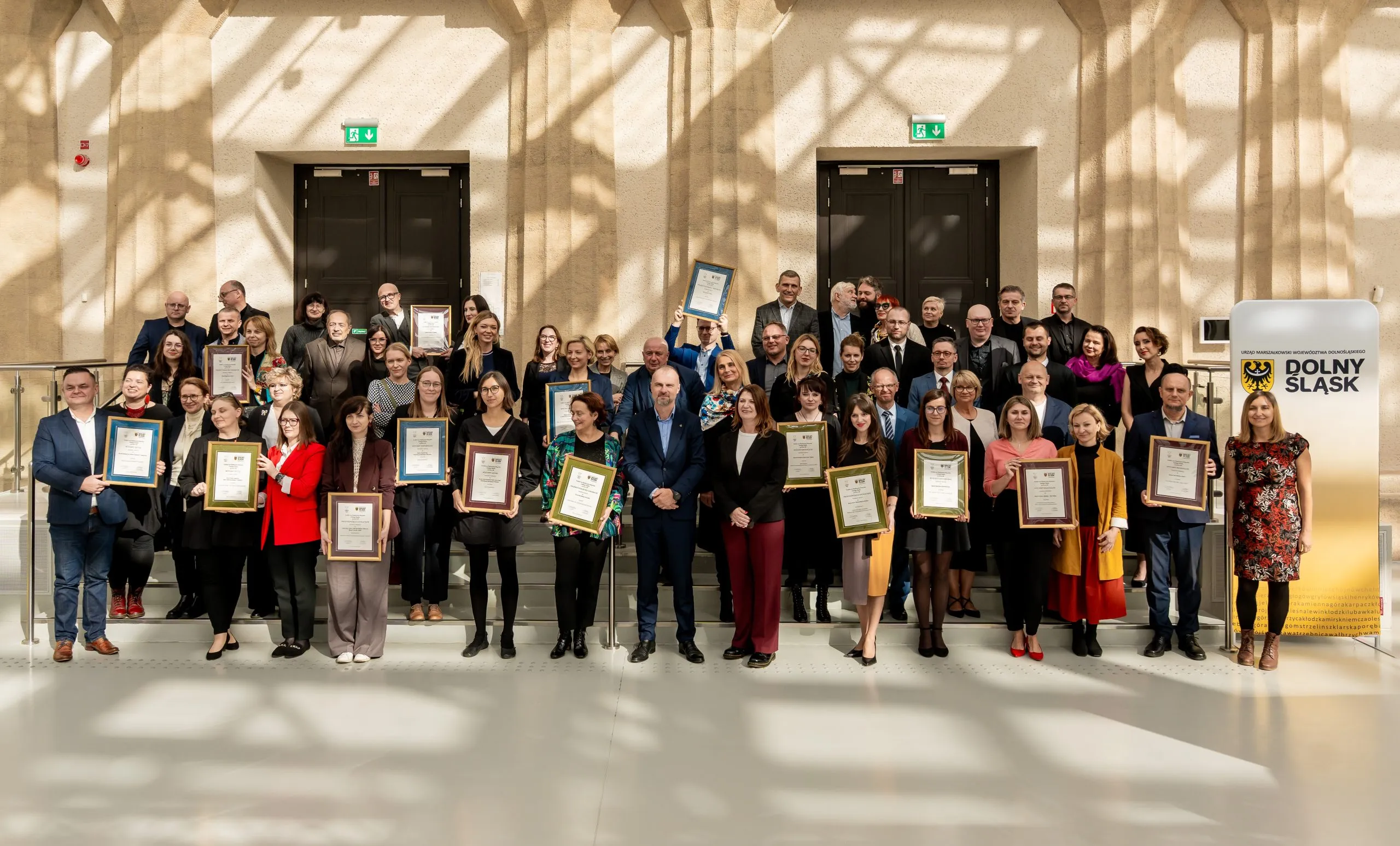 Velká skupina vítězů a organizátorů pózuje ve světlém sále a drží zarámované diplomy a ocenění předaná během muzejní soutěže.