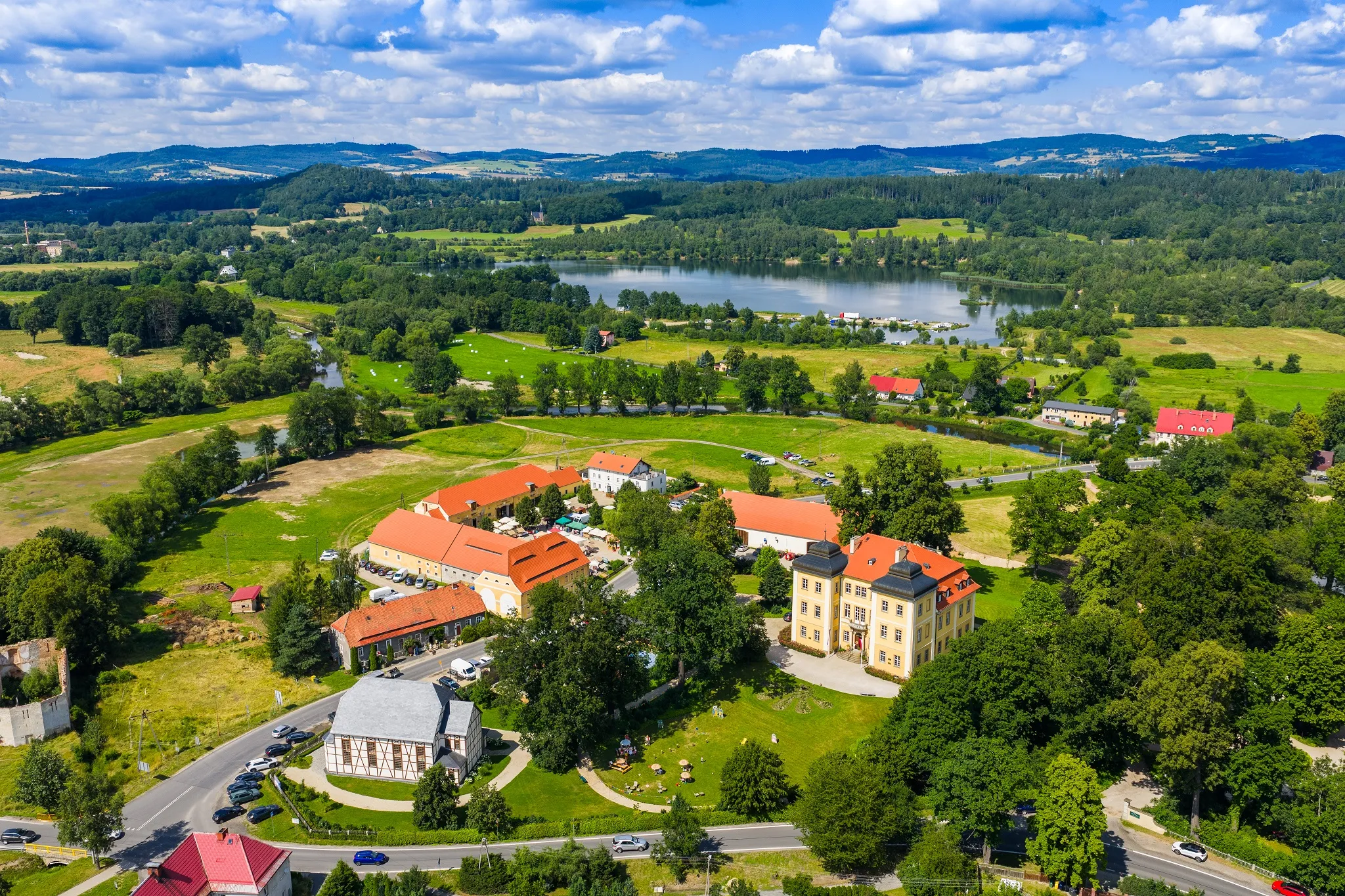 Widok z drona na na Pałac Łomncia wraz z folwarkiem i dominium z panoramą kotliny jeleniogórskiej w tle