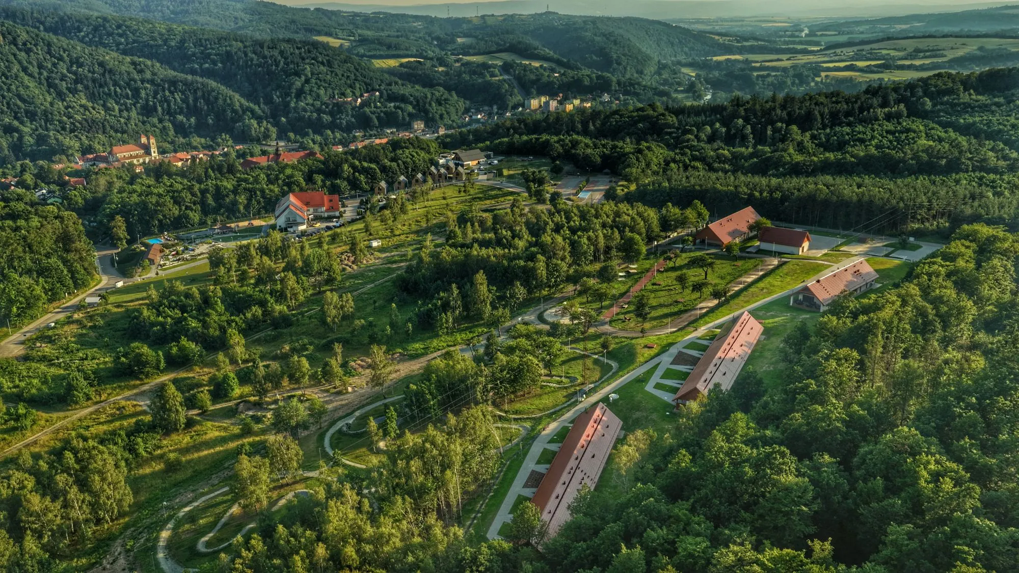 Pohled z dronu na ubytovací centrum na pozadí zeleně a kopců.